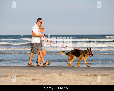 A middle aged caucasian couple walks a German Shepherd dog on the beach during golden hour in Port Aransas, Texas USA. Stock Photo