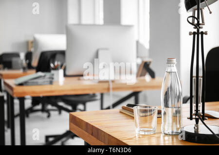 Workplace with bottle of water, lamp and notebook on table in modern office Stock Photo