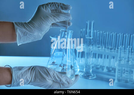 Scientist holding conical flask with liquid and pipette in laboratory Stock Photo