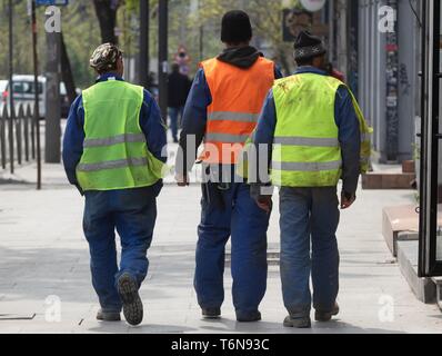 Bucharest, Romania - April 22, 2019: Three construction workers dressed in reflective working equipment walks on the sidewalk, in downtown Bucharest,  Stock Photo