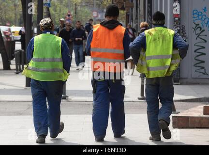 Bucharest, Romania - April 22, 2019: Three construction workers dressed in reflective working equipment walks on the sidewalk, in downtown Bucharest,  Stock Photo