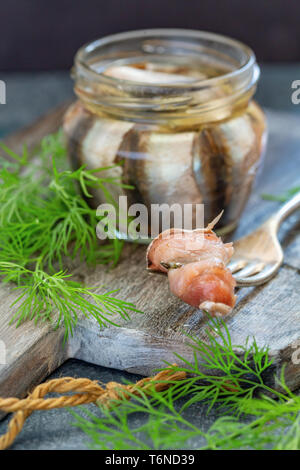 Salted fish on a fork and anchovies in jar. Stock Photo