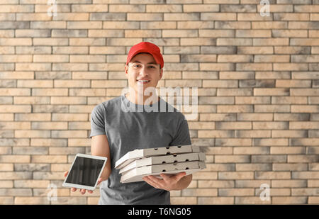 Delivery man with cardboard pizza boxes and tablet on brick wall background Stock Photo