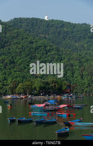 lakeside view of Phewa lake with many boats floating in the water and Shanti stupa on mountain peak. Pokhara, Nepal. Stock Photo