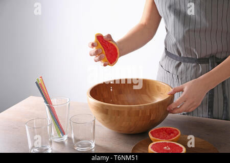 Woman squeezing citrus fruit over bowl on table Stock Photo