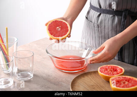 Woman squeezing citrus fruit over bowl on table Stock Photo