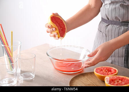 Woman squeezing citrus fruit over bowl on table Stock Photo