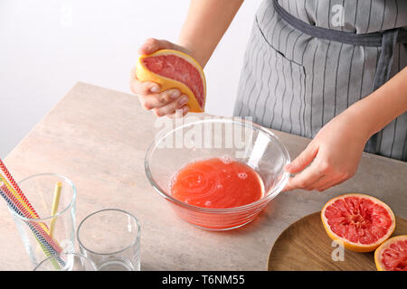 Woman squeezing citrus fruit over bowl on table Stock Photo