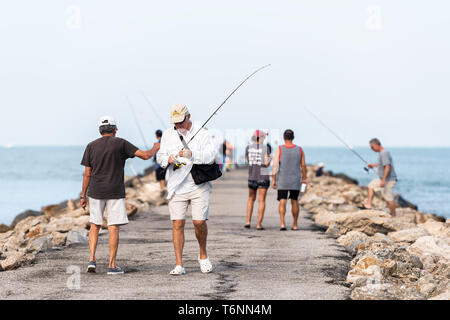 Venice, USA - April 29, 2018: Many people men standing fishermen fishing on rocky pier in Florida retirement beach town in gulf of Mexico with rods Stock Photo