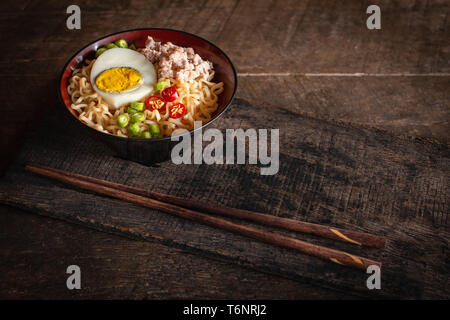 Instant noodle with pork, egg and vegetables on black bowl on the wood table there is chopstick placed in front of. Stock Photo