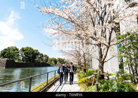Tokyo, Japan - April 1, 2018: Palace Hotel view of modern building by water in downtown with cherry blossom trees in spring and business men walking Stock Photo