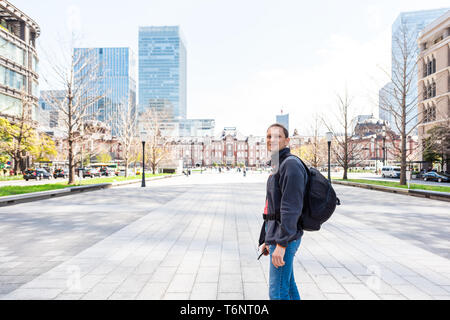 Tokyo Station building view in downtown with skyscrapers modern cityscape skyline and young tourist man with backpack standing happy in Japan Stock Photo