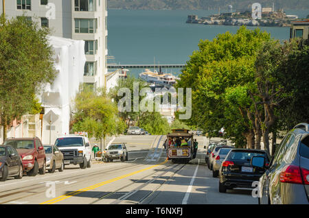 SAN FRANCISCO, CALIFORNIA - 2015, JUNE 24:  cable car, an iconic tourist attraction, descending a steep hill peak overlooking Alcatraz prison island a Stock Photo
