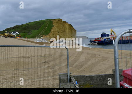 West Bay, Dorset, UK. 2nd May 2019. A large coastal defence is underway at West Bay in Dorset. Large blocks are delivered by boats and off loaded into the sea front by bucket loads. The stones come from Scotland where its picked up by large mechanical clasps and driven up the pebble beach. The sea front is where the TV show Broadchurch was filmed.Picture Credit: Robert Timoney/Alamy Live Newss Stock Photo