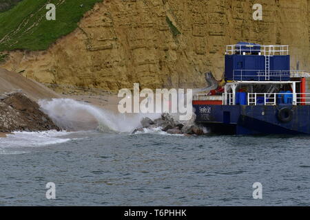 West Bay, Dorset, UK. 2nd May 2019. A large coastal defence is underway at West Bay in Dorset. Large blocks are delivered by boats and off loaded into the sea front by bucket loads. The stones come from Scotland where its picked up by large mechanical clasps and driven up the pebble beach. The sea front is where the TV show Broadchurch was filmed.Picture Credit: Robert Timoney/Alamy Live Newss Stock Photo