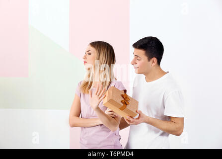 Offended young woman refusing to take gift from her boyfriend on light background Stock Photo