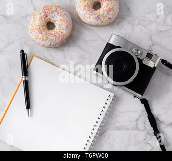 Flat lay with donuts, flowers, camera and notepad on white marble background. Summer concept. Stock Photo