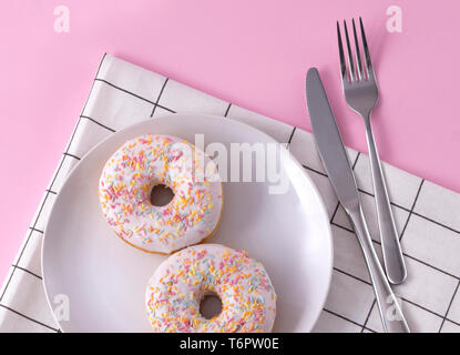 Delicious donuts on the plate with napkin and cutlery at pink background. Stock Photo