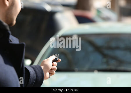 Man pushing button on remote control of car alarm system, outdoors Stock Photo