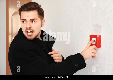 Young man pushing button of fire alarm system, indoors Stock Photo