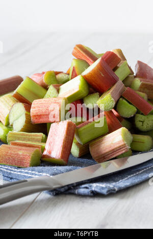 Pile of sliced rhubarb and knife on a blue tea towel with a grey wood background Stock Photo