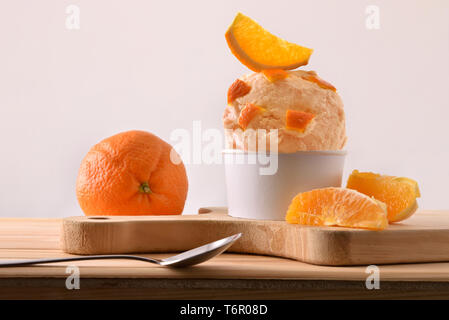Orange ice cream cup decorated with orange segments on a wooden table. Horizontal composition. Front view. Stock Photo