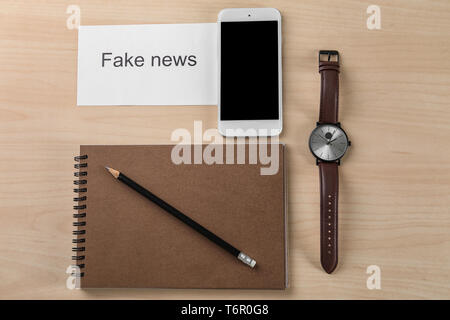 Composition with phrase FAKE NEWS and phone on wooden background Stock Photo