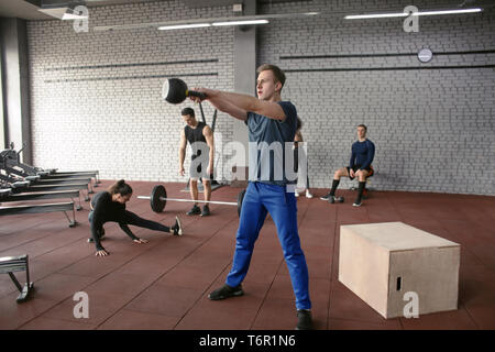 Athletic man doing exercises with kettlebell in modern gym Stock Photo