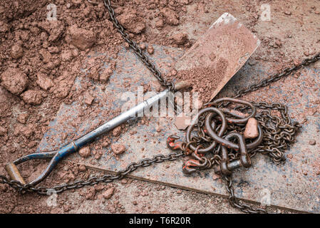 A builders' spade, heavy metal chains, rain and mud. Still life on a building site Stock Photo