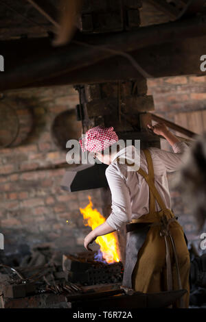 Rear view of isolated female worker, in overalls & headscarf inside nail shop at Black Country Living Museum, UK, making nails in industrial workshop. Stock Photo