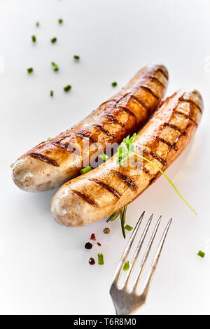 Two grilled sausages and a fork in close-up, served on white dish with leaf of fresh parsley and spices and viewed from above Stock Photo
