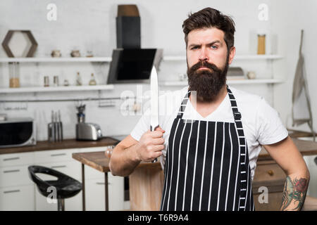 Kitchen equipment. culinary business. tasty cuisine. serious and confident chef in restaurant. bearded man hipster in kitchen with knife. brutal man in cook apron. mature male with beard cooking. Stock Photo