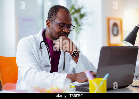 Dark-skinned doctor wearing glasses and watch feeling thoughtful Stock Photo