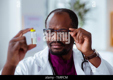 Doctor wearing glasses looking at ampoule checking the liquid Stock Photo