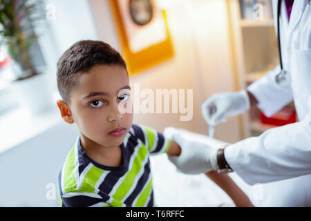 Dark-eyed preschool boy visiting pediatrician having injection Stock Photo
