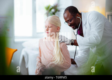 Dark-skinned doctor listening to lungs of girl using stethoscope Stock Photo