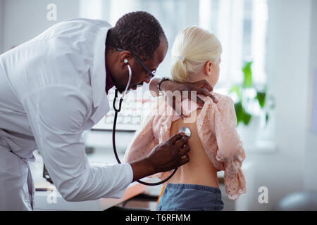 Dark-skinned pediatrician using stethoscope while examining girl Stock Photo