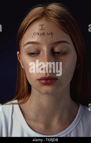 Portrait of young woman with mental health problems. The image of a tattoo on the forehead with the words I gave up. Concept of hidding the true feelings, psycological trouble, treatment. Stock Photo