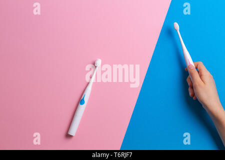 Kid hand with electric toothbrushes on pink and blue background Stock Photo