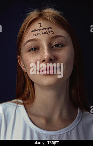 Portrait of young woman overcoming mental health problems. Tattoo on the forehead with the words I want to die-happy. Concept of psycological treatment, rehabilitation, return to healthy lifestyle. Stock Photo