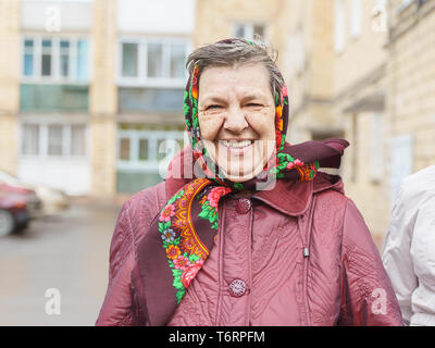 Senior woman in a headscarf is smiling in the street in the courtyard among high-rise buildings Stock Photo