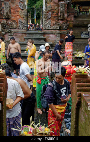 Tourist taking photo on cell phone of worshippers cleansing at Tampak Siring, the Holy Spring Water Temple near Ubud in Bali, Indonesia Stock Photo