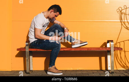 Colorful portrait of a handsome man in white t-shirt and jeans with phone on the yellow background Stock Photo