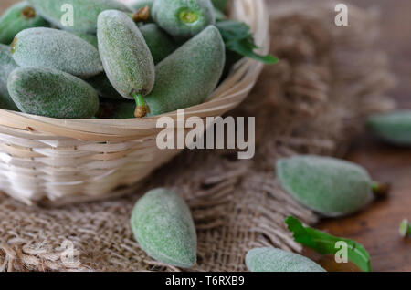 Fresh green unripe almonds in basket on wooden table Stock Photo