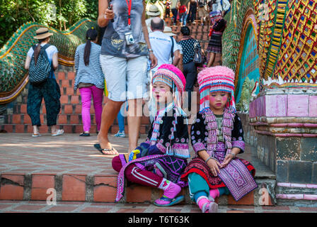 Chiang Mai, Thailand - Dec 2015: Tribal girls dressed in traditional dress sitting at the stairs and looking sad in front of Doi Suthep temple entranc Stock Photo