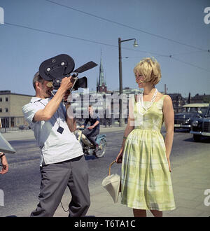 Woman in the 1960s. A Young blond woman is being filmed when standing in the street. A camera man with a film camera is standing beside her filming. She is wearing a typical 1950s skirt. Sweden 1950s early 1960s Stock Photo