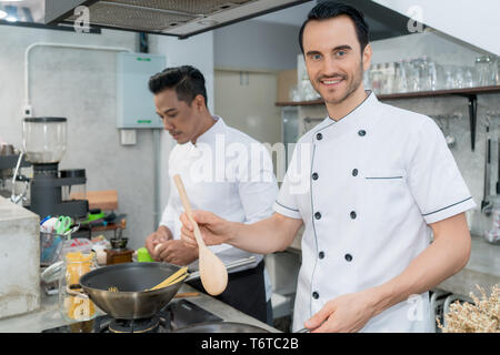 Portrait of young male chef preparing spaghetti with colleague in kitchen. Stock Photo