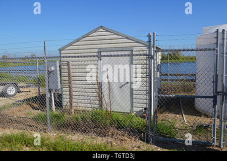 Outdoors Day Time Close-up View of Small Locked Metal Storage Shed Exterior Barbed Wire Enclosed Secure Protected Industrial Business Fenced In Area Stock Photo