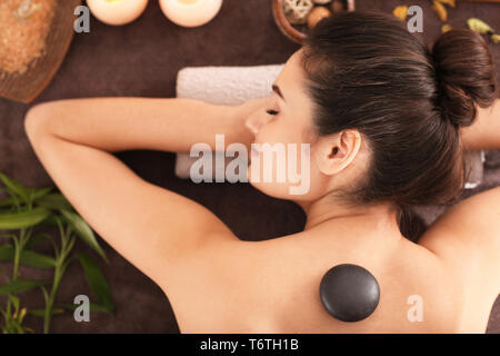 Young woman undergoing hot stone therapy on massage table at spa salon, top view Stock Photo