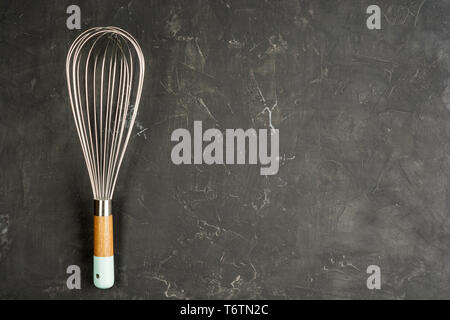 Kitchen Wire Whisk Eggs Beater on the dark concrete background with copy space. Flat lay background. Stock Photo